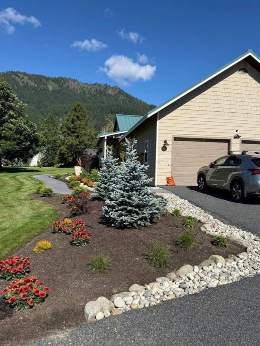 Finished landscape bed near garage with blue spruce and river rock after service