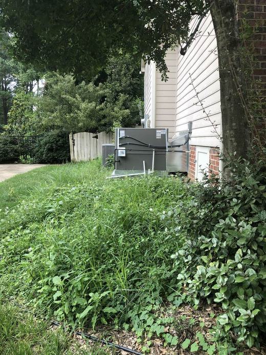 Overgrown grass around AC unit before service